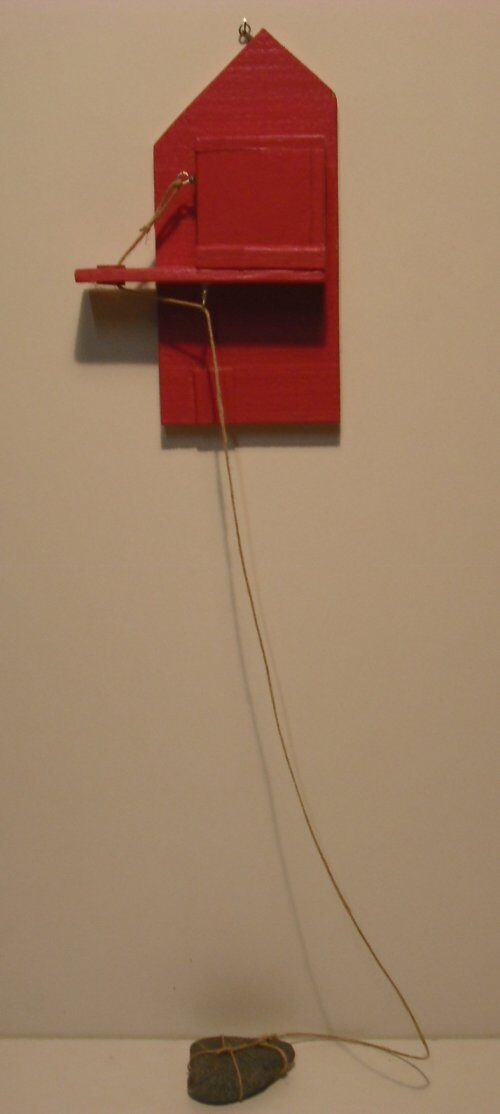 Papier rouge en forme de maison, avec une petite porte et un petit escalier, suspendu à un fil de fer
